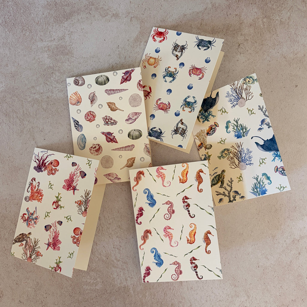 Five small gift cards with colorful undersea-themed illustrations, including crabs, seahorses, and sea plants, arranged on a textured beige surface. Printed on textured ivory paper. 