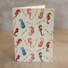 Five small gift cards with colorful undersea-themed illustrations, including crabs, seahorses, and sea plants, arranged on a textured beige surface. Printed on textured ivory paper. 