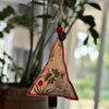 Decorative triangle hanging ornament with floral design and beads against a blurred greenery background
