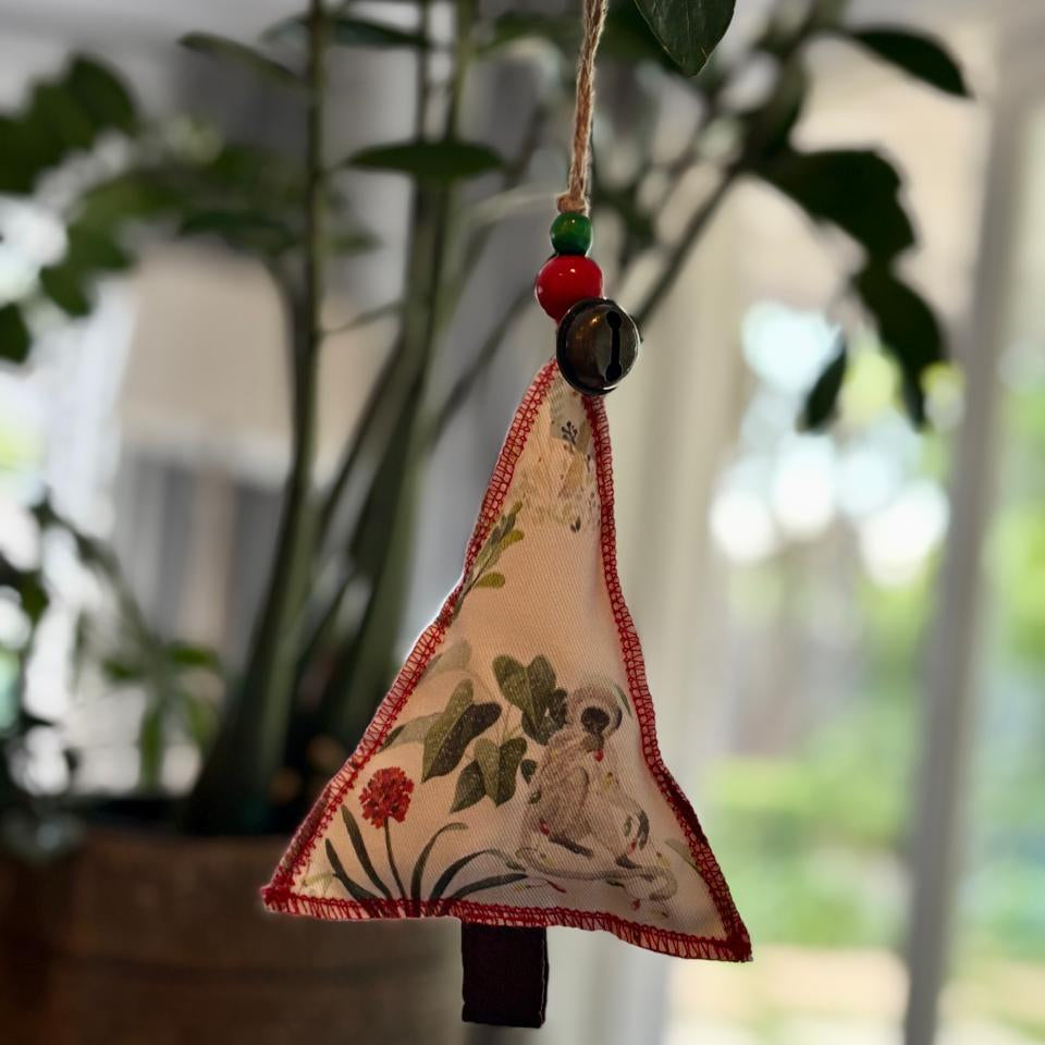Decorative triangle hanging ornament with floral design and beads against a blurred greenery background
